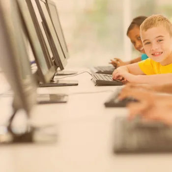 Élèves souriants devant des ordinateurs dans une salle informatique