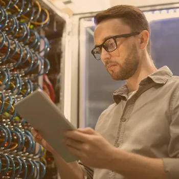 Technicien consultant une tablette devant une baie de serveurs