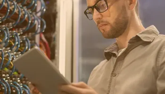 Technicien consultant une tablette devant une baie de serveurs